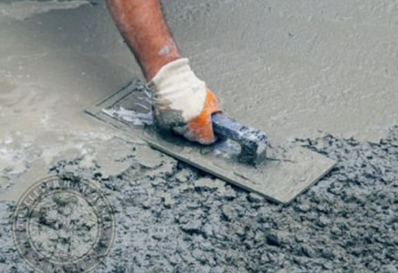 a person applying a coat of cement which is an artificial construction material on the floor