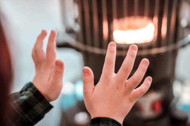 ہیٹر کے آگے بیٹھے گرمائش لیتے ایک چھوٹے بچے کے ہاتھ